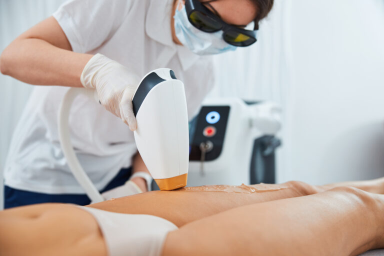 Focused beautician with a laser device in her hand leaning over a young Caucasian woman