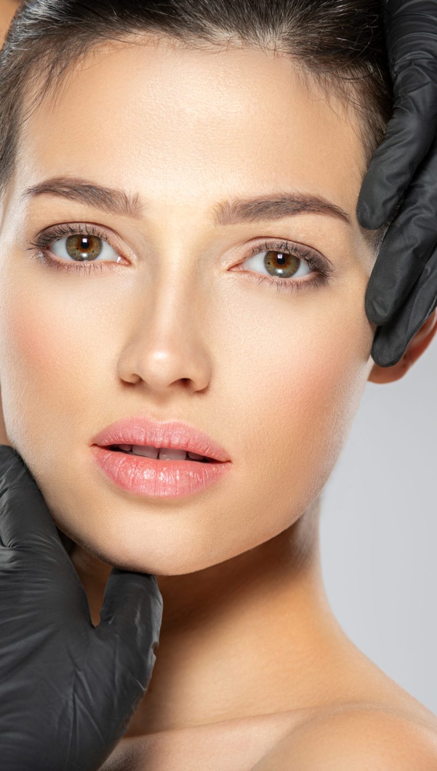 Woman is touching her face before plastic surgery. Adult girl checks a skin before botox injection. Beauty treatments. White woman in the black medical gloves. Face skin check before plastic surgery.